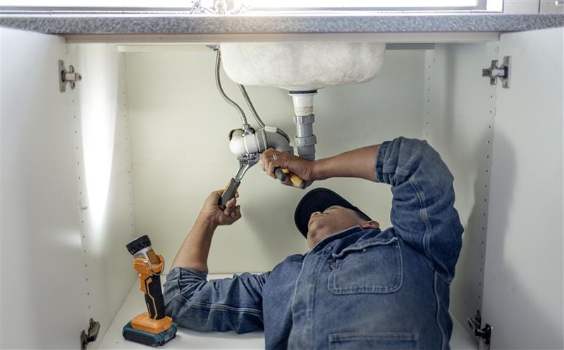 Plumber repairing pipes beneath a bathroom sink in Immokalee