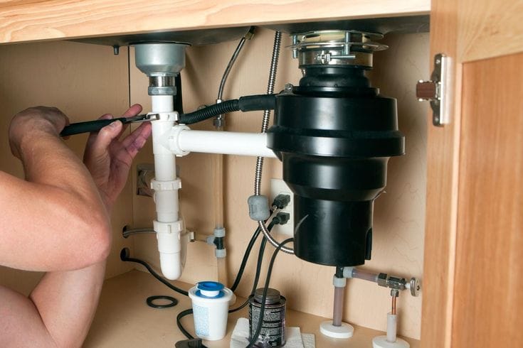 Plumber installing a garbage disposal beneath a kitchen sink in Immokalee